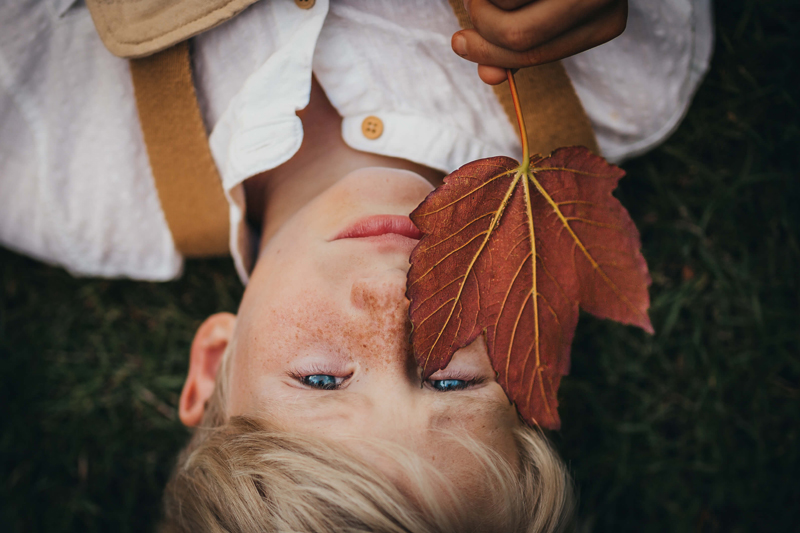 London Family Photographer, boy laying on his back holding a leave over his face
