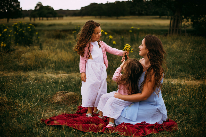 London Family Photographer, mother and two young daughters sitting on a blanket outside