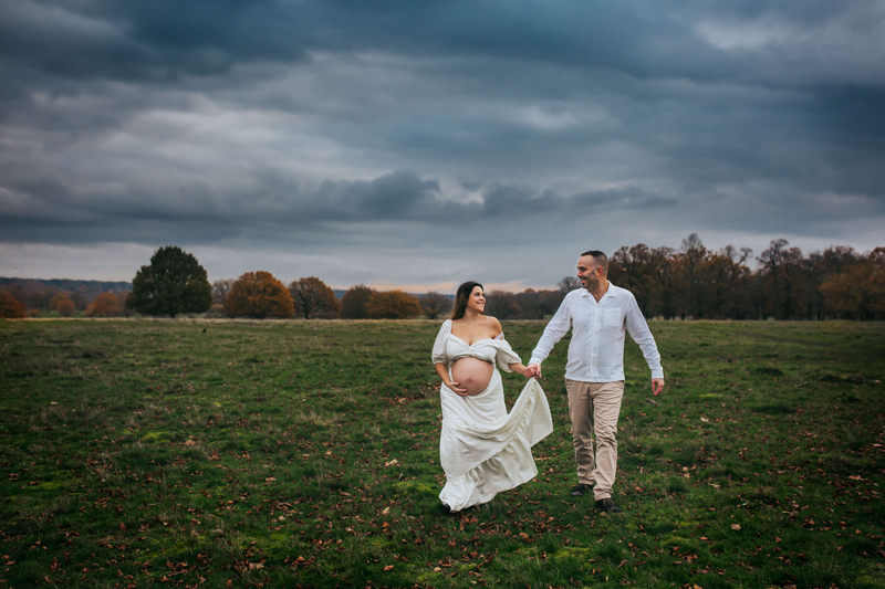 London Family Photographer, pregnant woman walking in a field, holding hands with baby's father