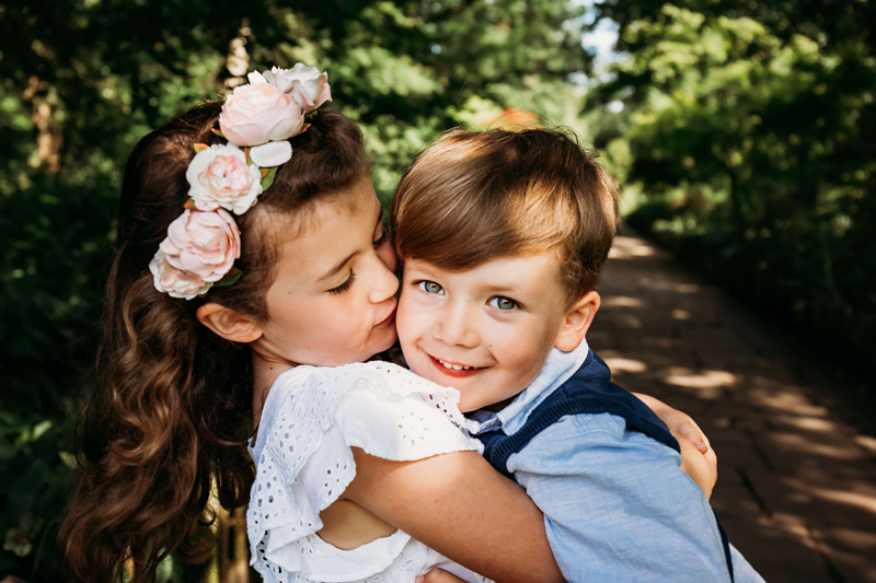 London Family Photographer, young brother and sister siblings hugging, with the sister kissing brother on the cheek